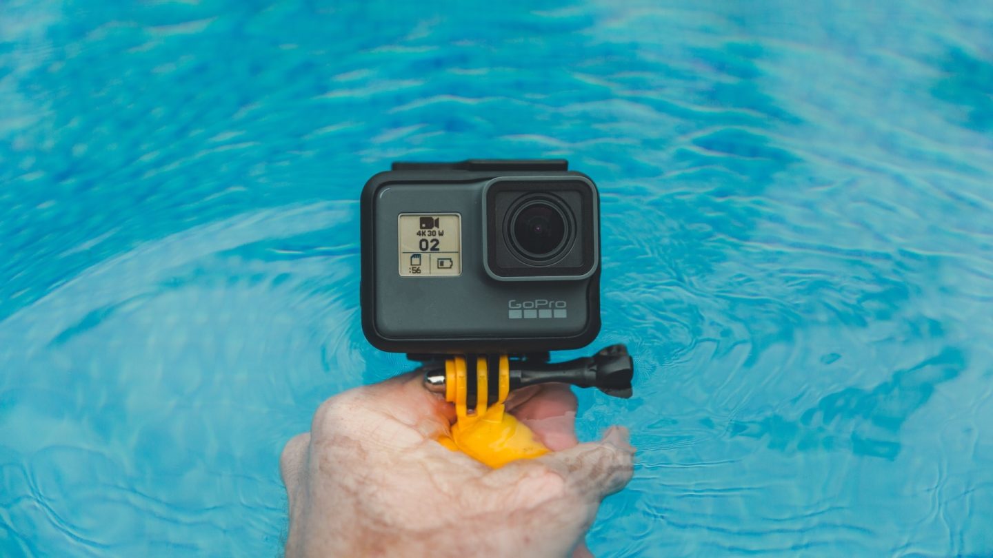 En hand håller upp en GoPro-actionkamera i en pool.