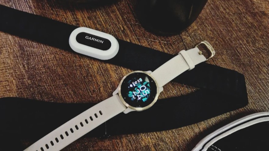 Garmin pulsband ligger på ett trägolv tillsammans med en Garmin Venu 3.