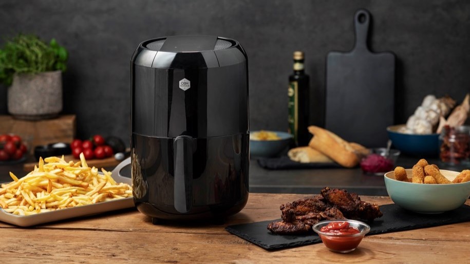 En svart OBH Nordica airfryer står på en köksbänk bland färdig mat som pommes, mozzarellasticks, revben och mer.
